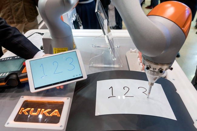 ブースでは「LBR iiwa」がタブレットに書いた文字をロボットが書くデモを展示